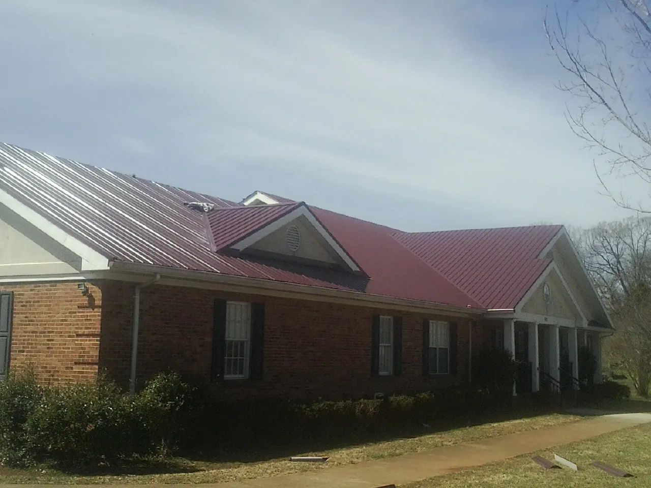 Red metal roof with gabled entries on a long brick building, from a Hail Damage Roof Repair job in Christmas