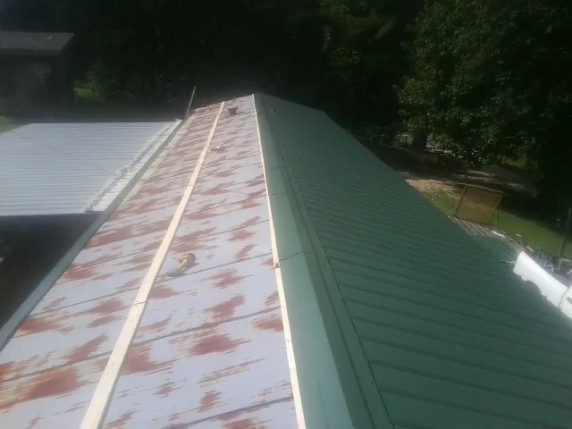 Old rusted panels beside newly installed green metal roofing — Wind Damage Roof Repair by Roofing Brothers in Christmas