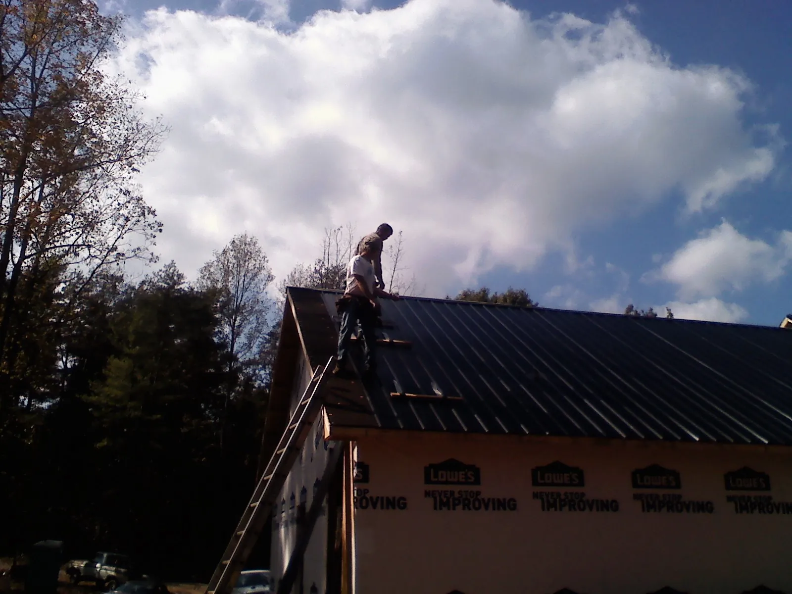 Roofer fastening dark metal panels high against a cloudy sky, from a Roof Inspection job in Christmas