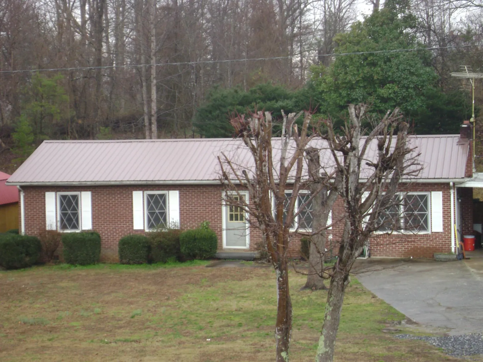Mauve metal roof on a brick ranch home behind bare trees in Christmas