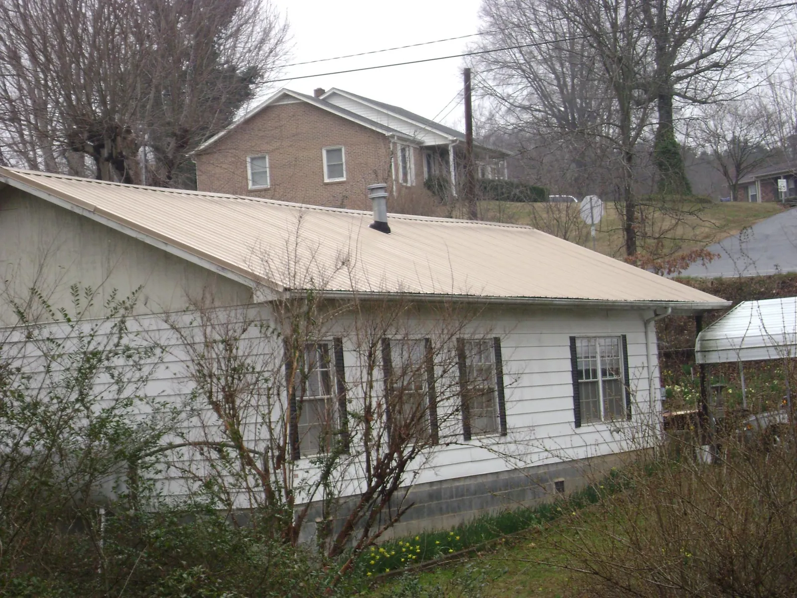 Tan metal roof on a white sided house set into a hillside — Commercial Roofing by Roofing Brothers in Christmas